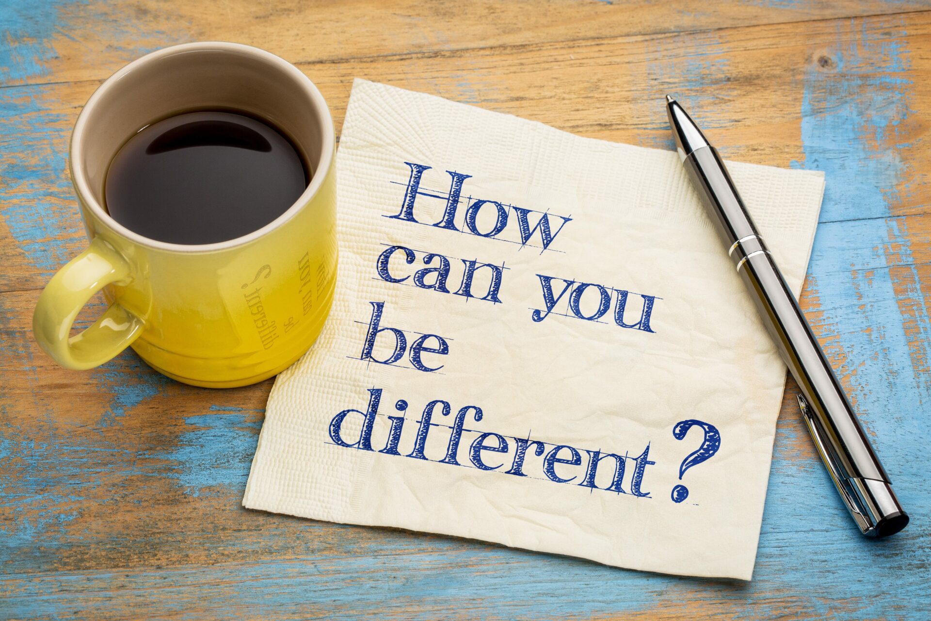 Branding question “How can you be different?” written on a napkin with a yellow mug of espresso coffee